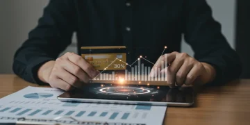 Hand holding credit card with tablet showing credit utilization below 30%